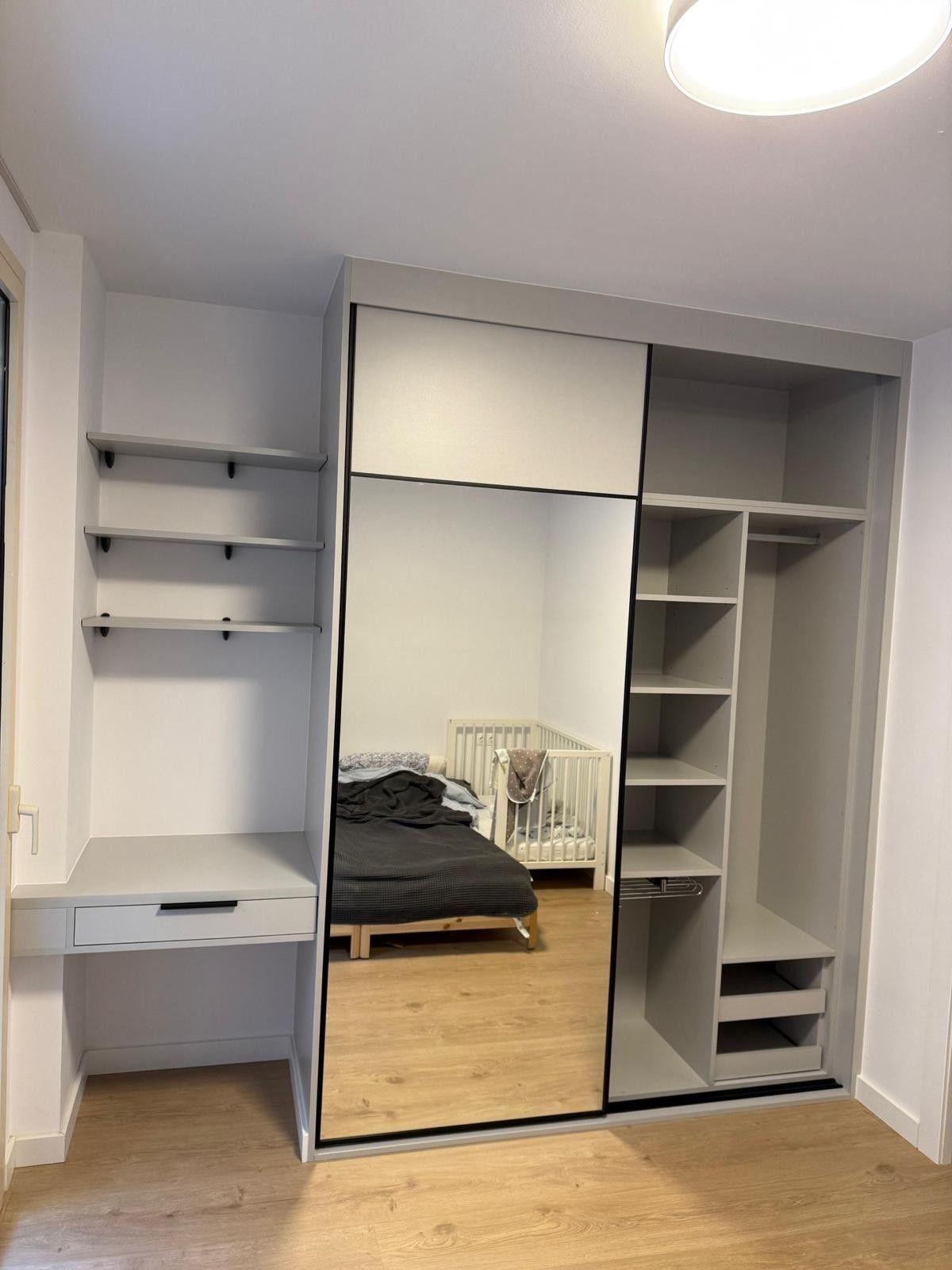 Armario empotrado gris con puertas de espejo y estantes en un dormitorio pequeño.