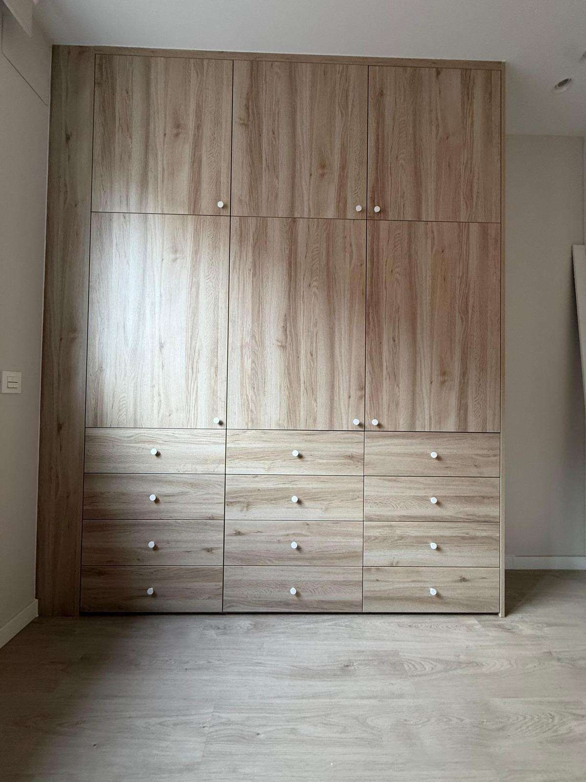 Amplio armario empotrado de madera clara con cajones en una habitación vacía.