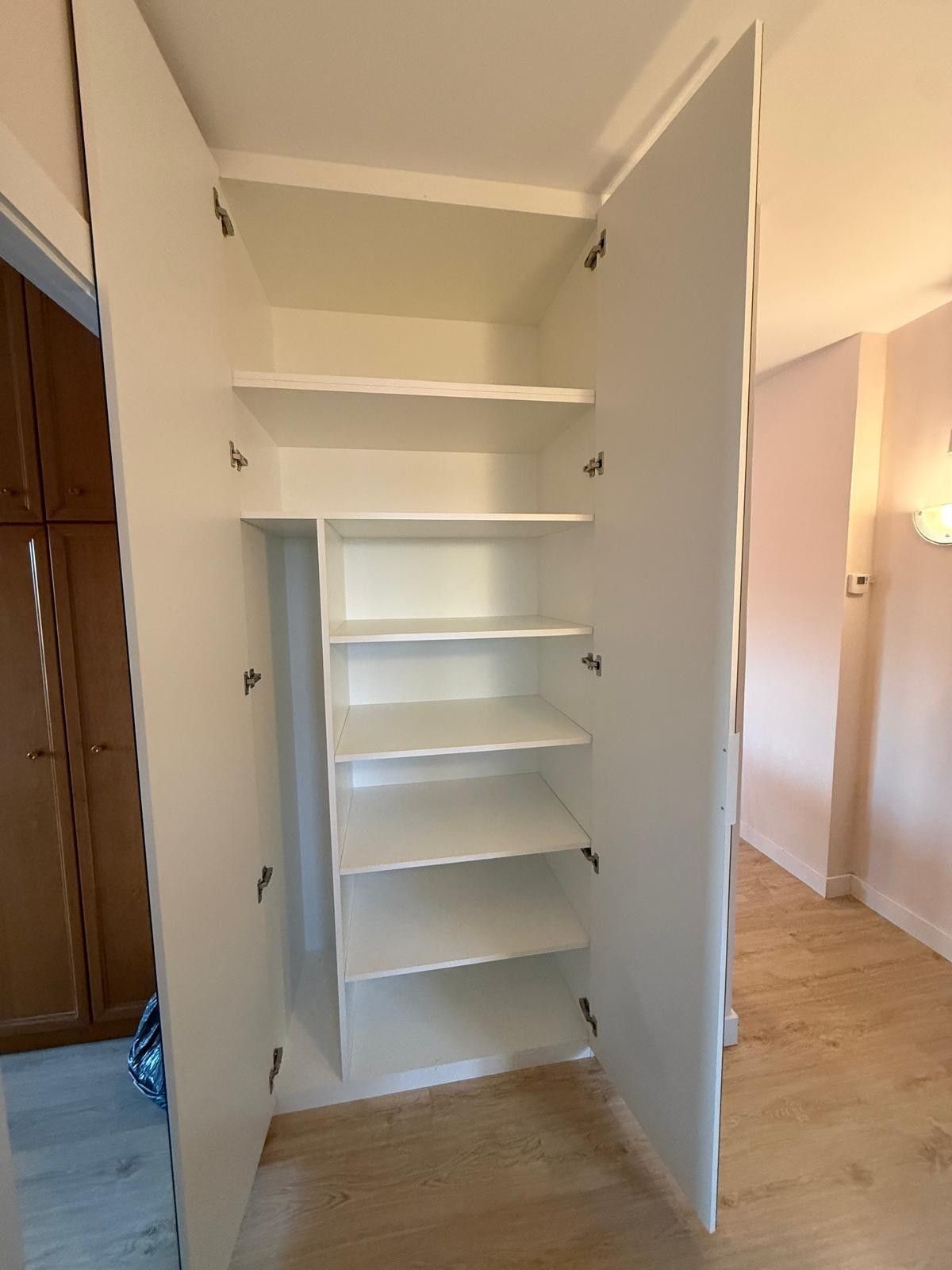 Armario blanco abierto con estantes empotrados en una habitación luminosa.