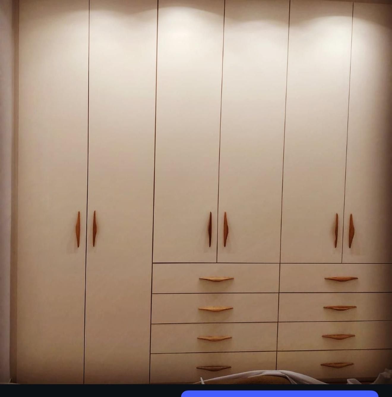 Armario empotrado beige con armarios, cajones y tiradores verticales largos en un dormitorio.