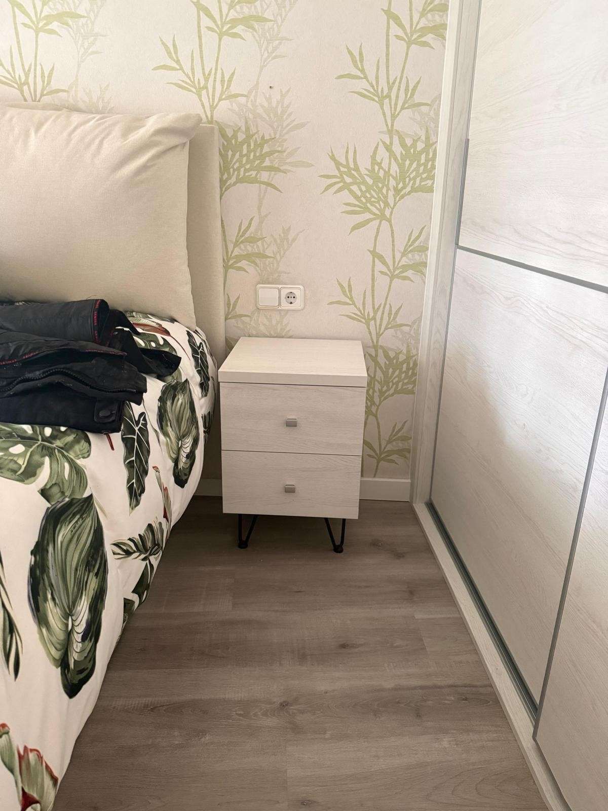 Pequeño rincón de dormitorio con una mesita de noche blanca junto a la cama y una puerta corredera de armario.