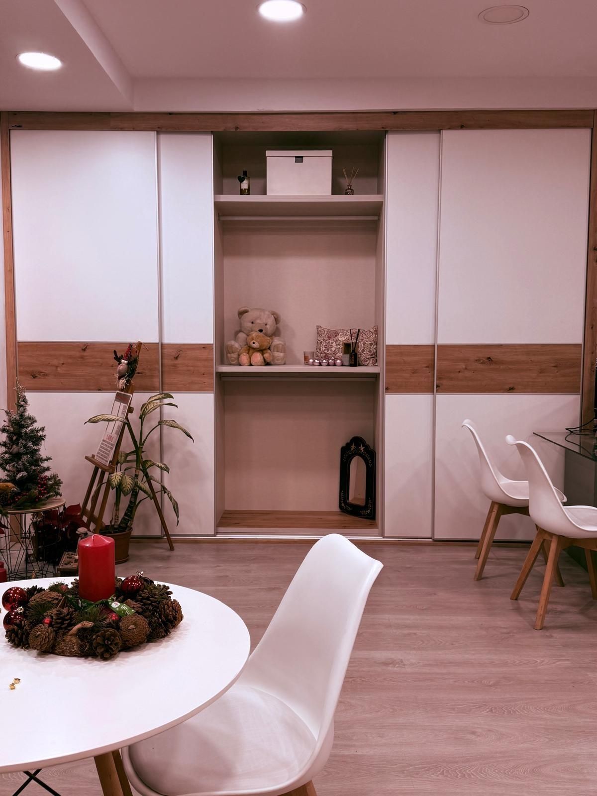 Sala de estar moderna con gabinetes blancos, detalles de madera, mesa redonda, sillas y un pequeño árbol de Navidad.