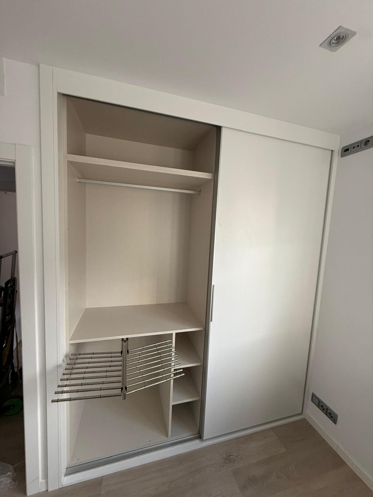 Armario empotrado blanco con puertas correderas, estantes abiertos y percheros extraíbles de alambre