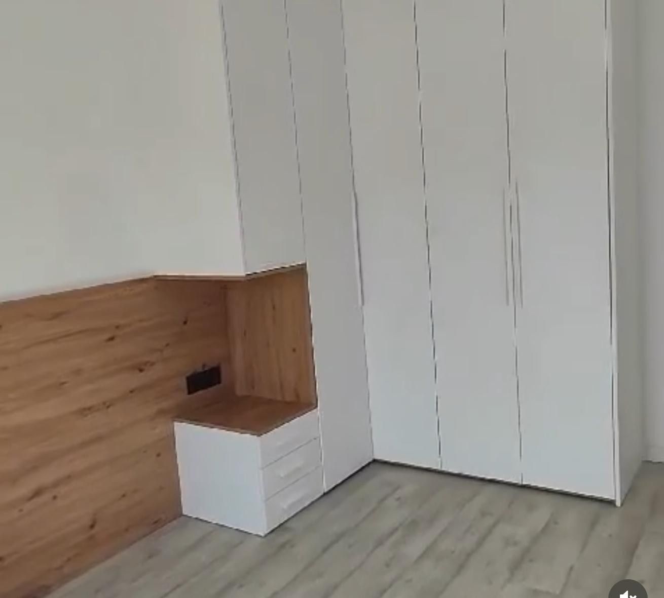 Habitación minimalista y vacía con armarios blancos, pared revestida de madera y suelo de madera clara.