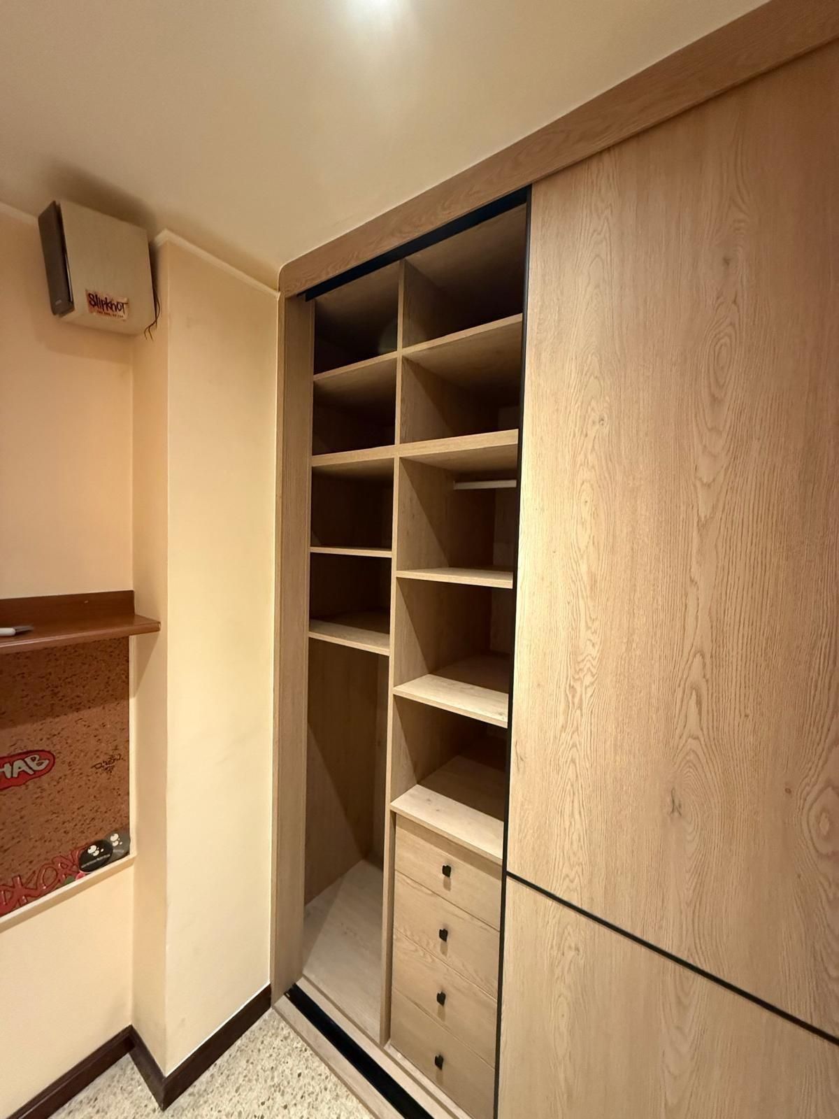 Armario empotrado de madera con estantes y cajones en un pasillo o habitación de color beige.