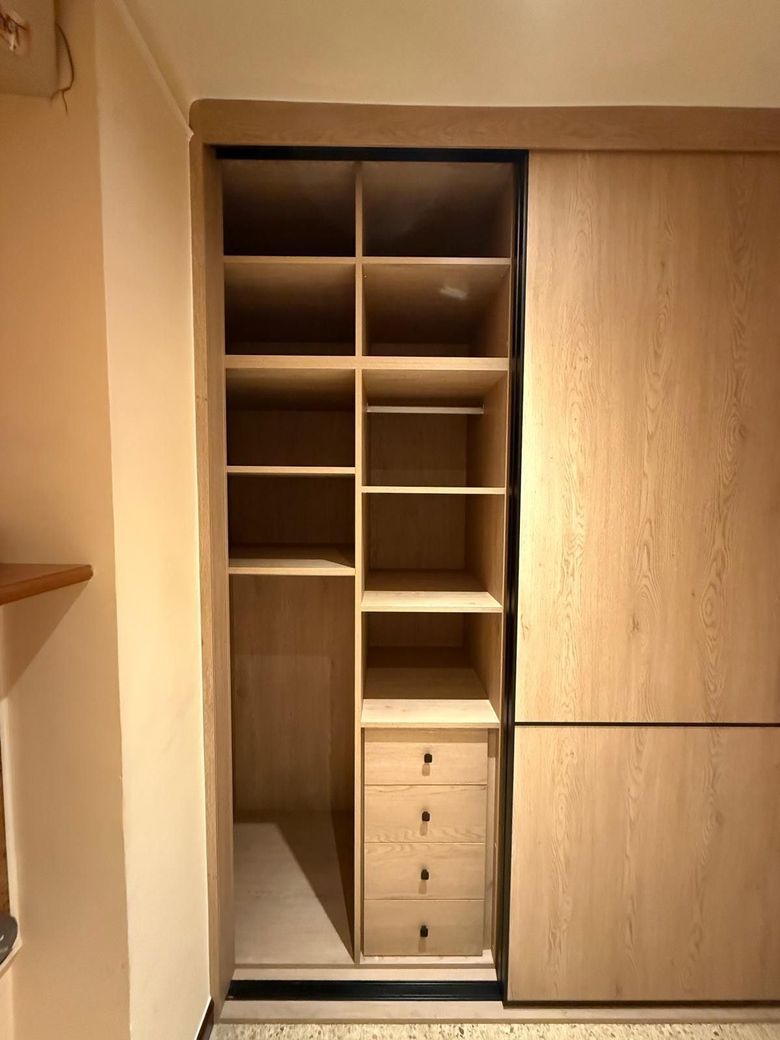 Armario empotrado de madera con estantes, espacio para colgar ropa y cajones, parcialmente abierto en una habitación.