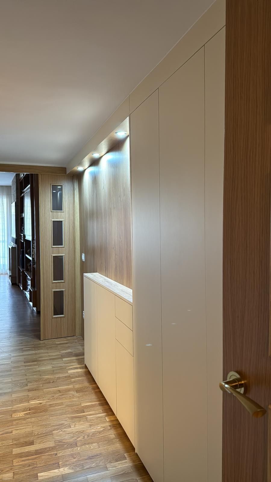 Pasillo moderno con suelo de madera, armarios blancos empotrados e iluminación empotrada a lo largo de la pared.