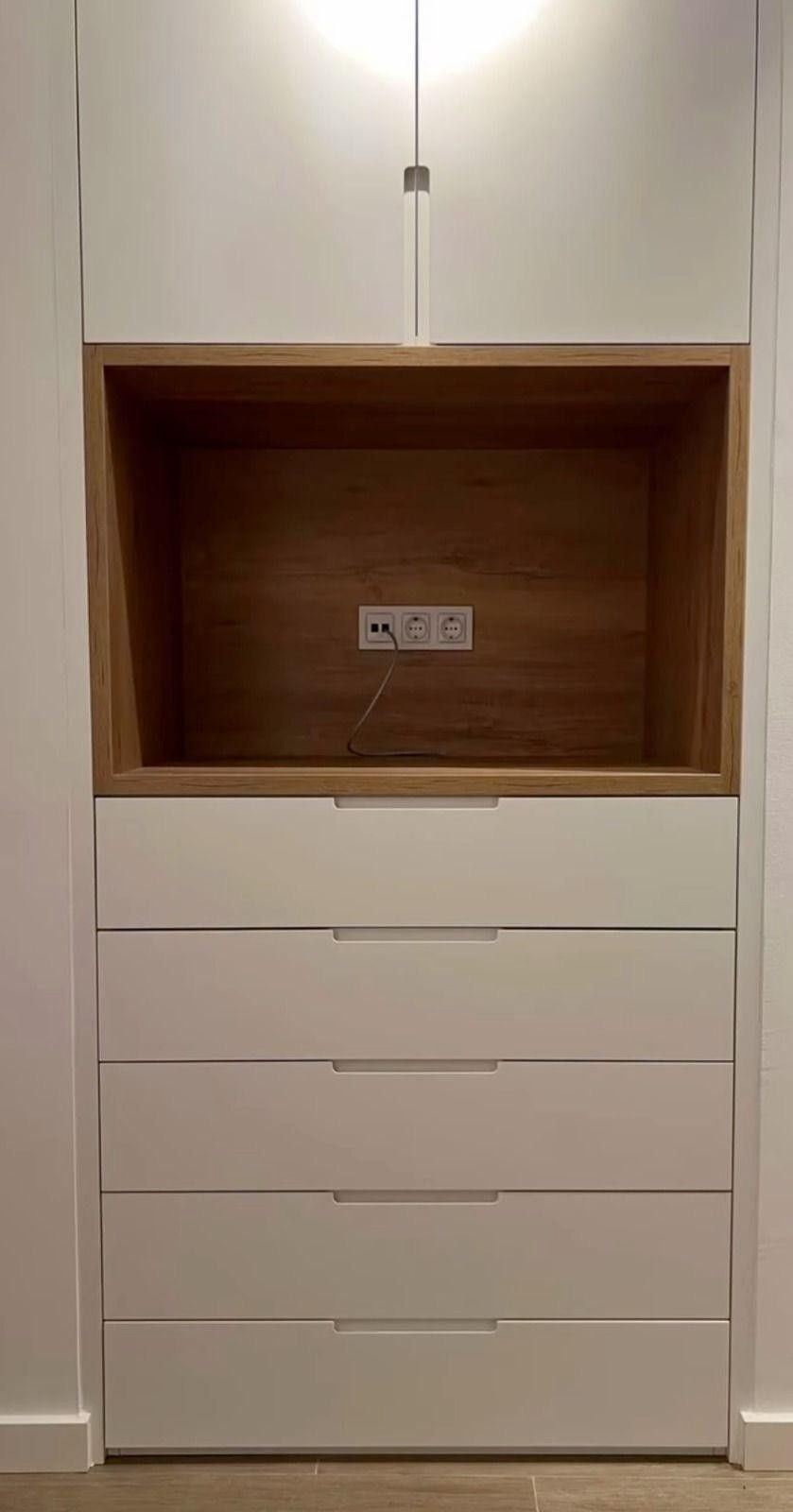 Cómoda blanca empotrada con compartimento de madera abierto y cinco cajones debajo de una lámpara de cable colgante.