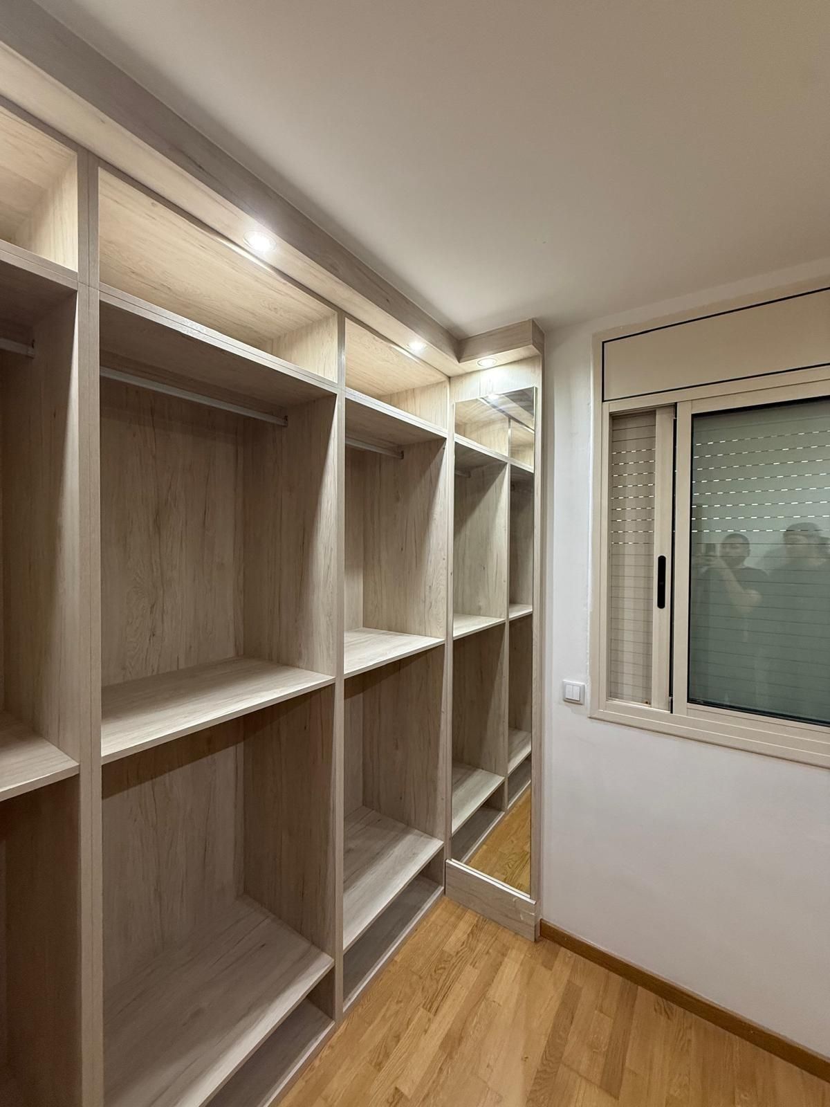 Vestidor vacío con estantes empotrados, suelo de madera y una ventana con la persiana cerrada.