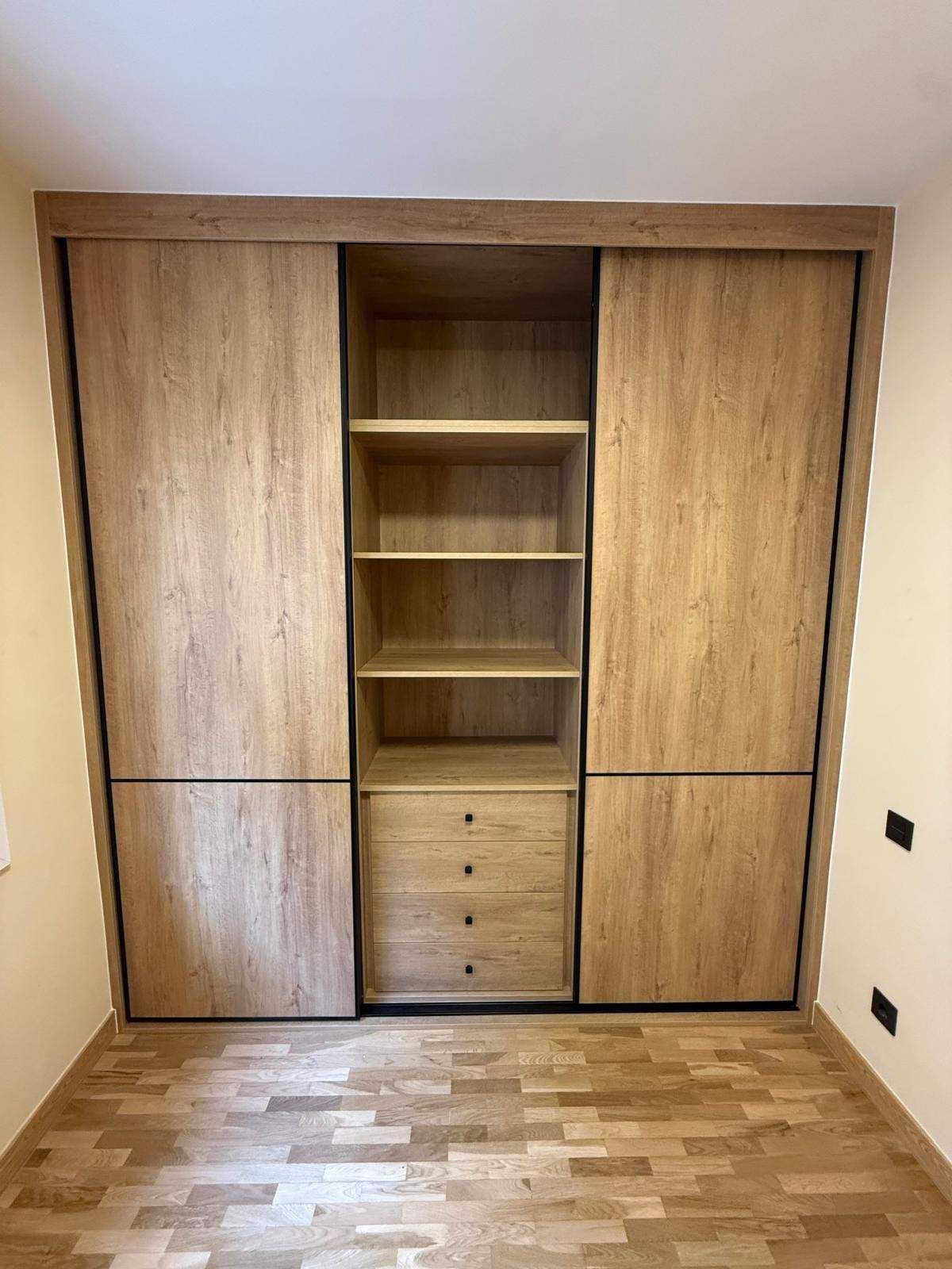 Armario empotrado de madera con estantes y cajones en una habitación pequeña con suelo de parqué.