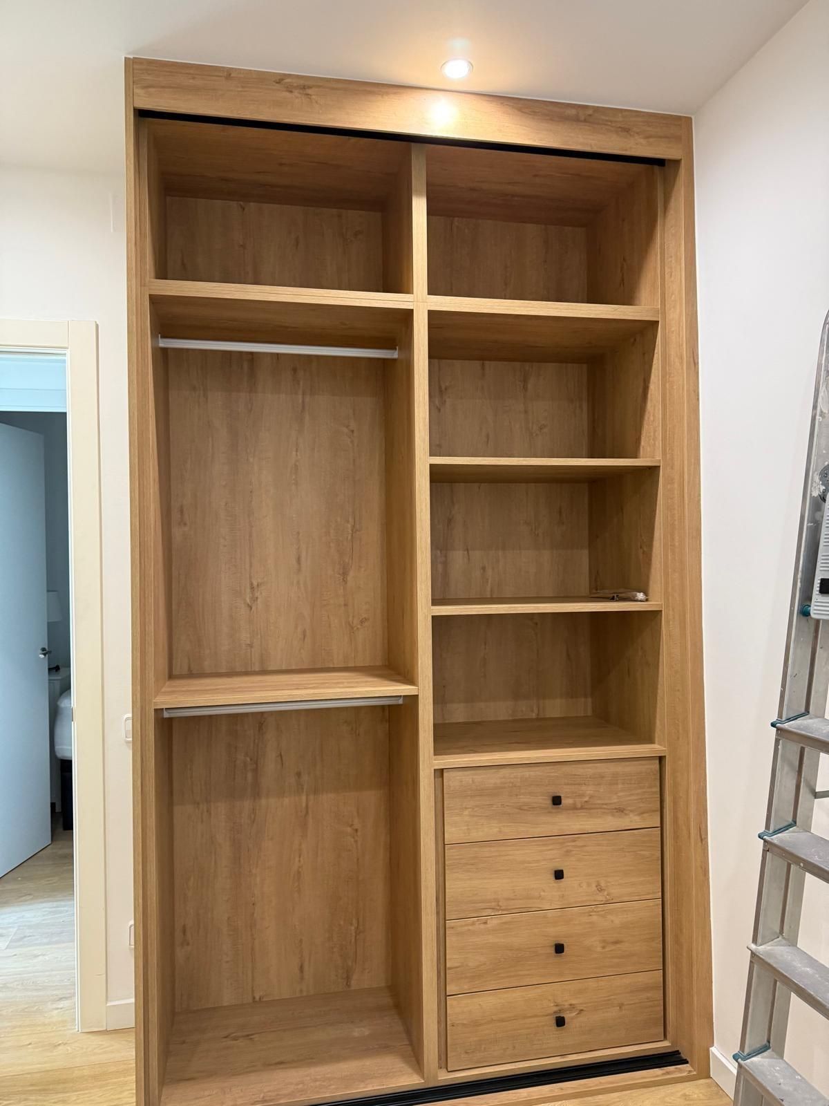 Armario empotrado de madera con estantes, espacio para colgar ropa y cajones en una habitación en construcción.