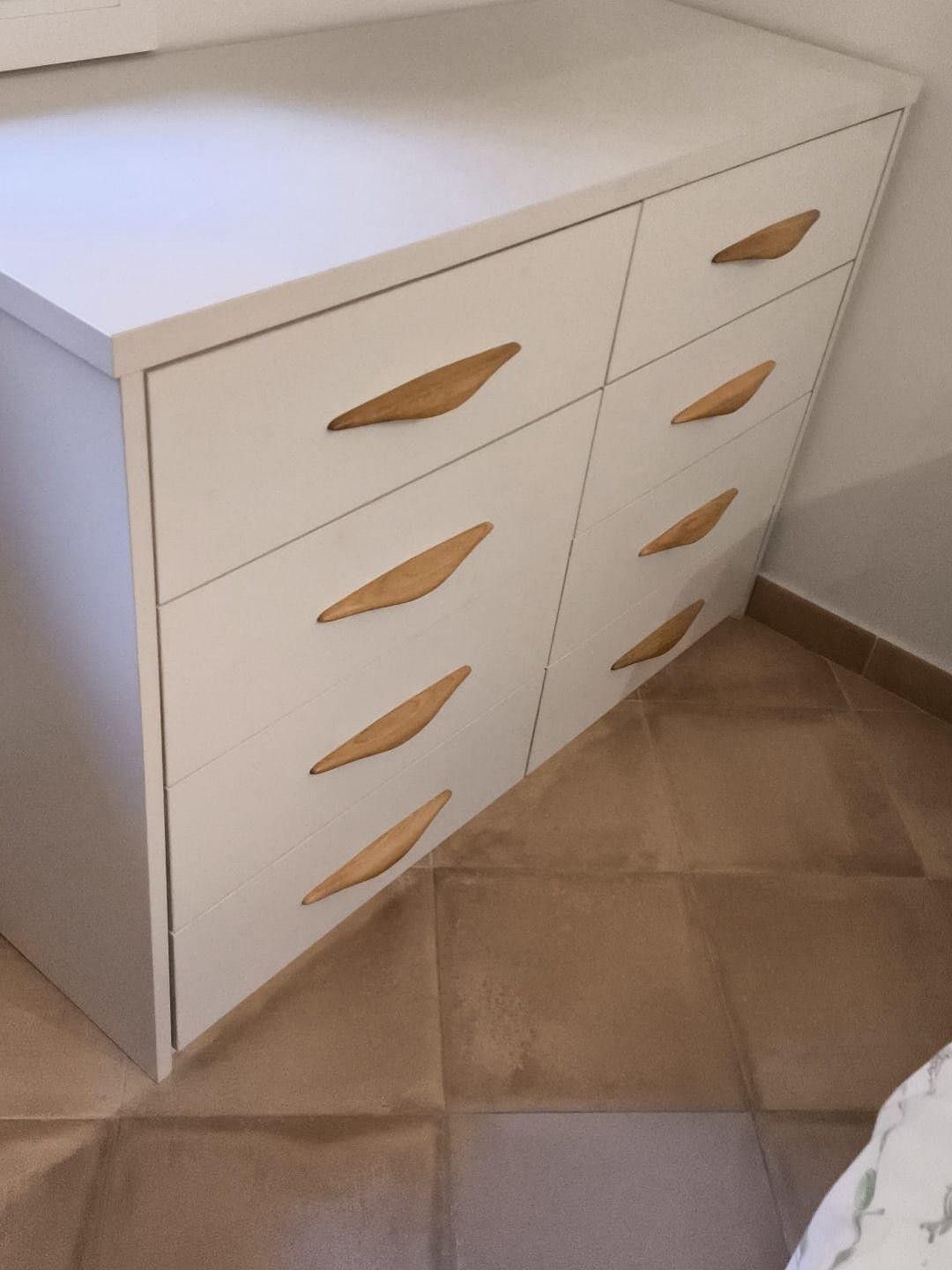 Cómoda blanca con tiradores de madera en un rincón alicatado junto a una pared.