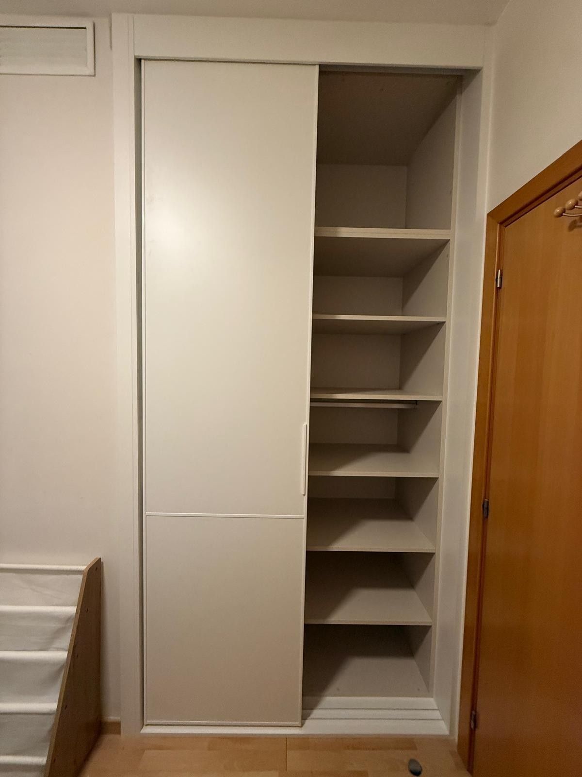Armario empotrado blanco con estantes abiertos y puerta corredera en un dormitorio.