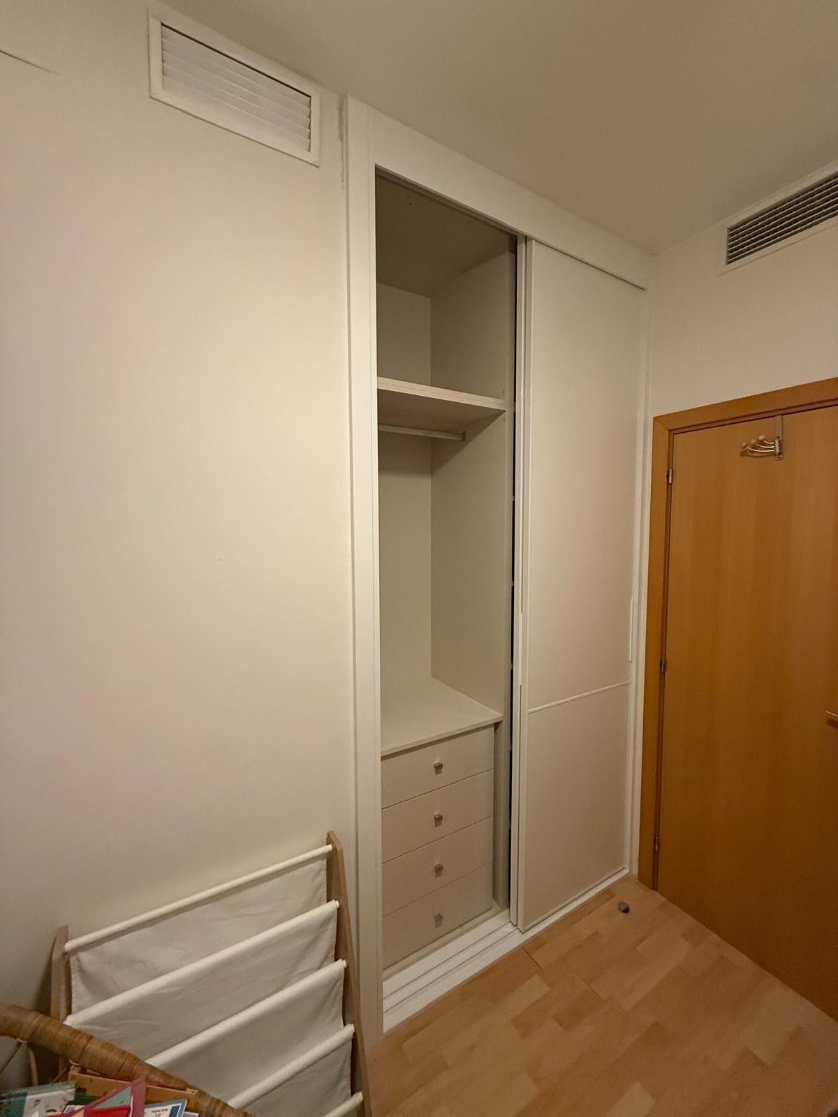 En una habitación pequeña, hay un armario blanco abierto con estantes y cajones