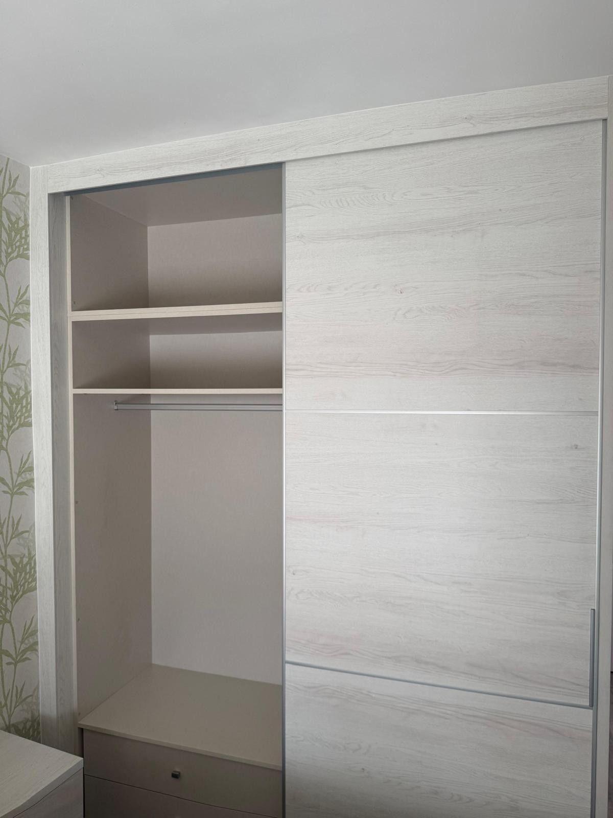 Armario abierto con puertas correderas blancas, estante, barra para colgar ropa y cajones inferiores en un dormitorio.