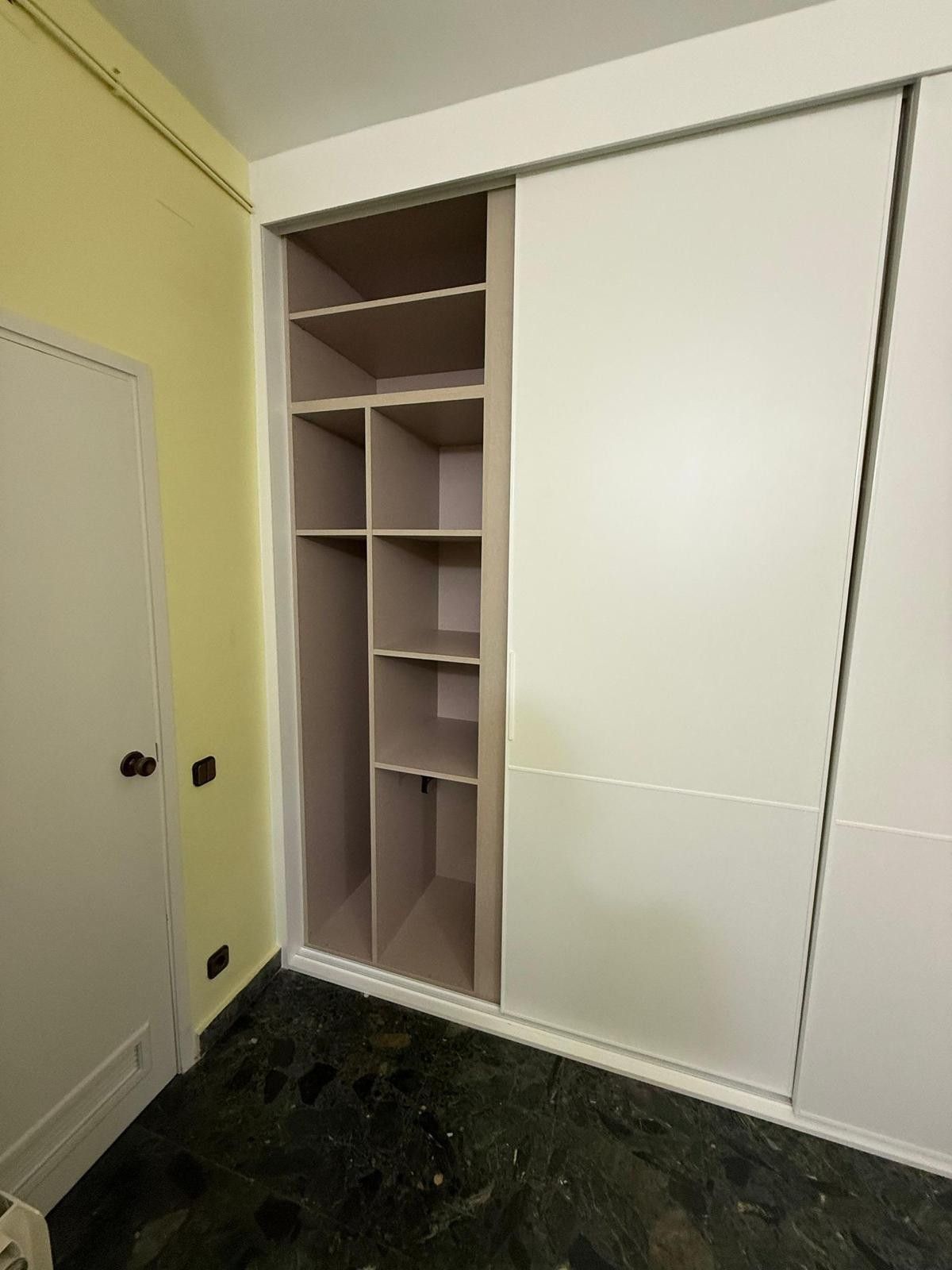 En una habitación pequeña, hay un armario blanco corredero con estantes abiertos