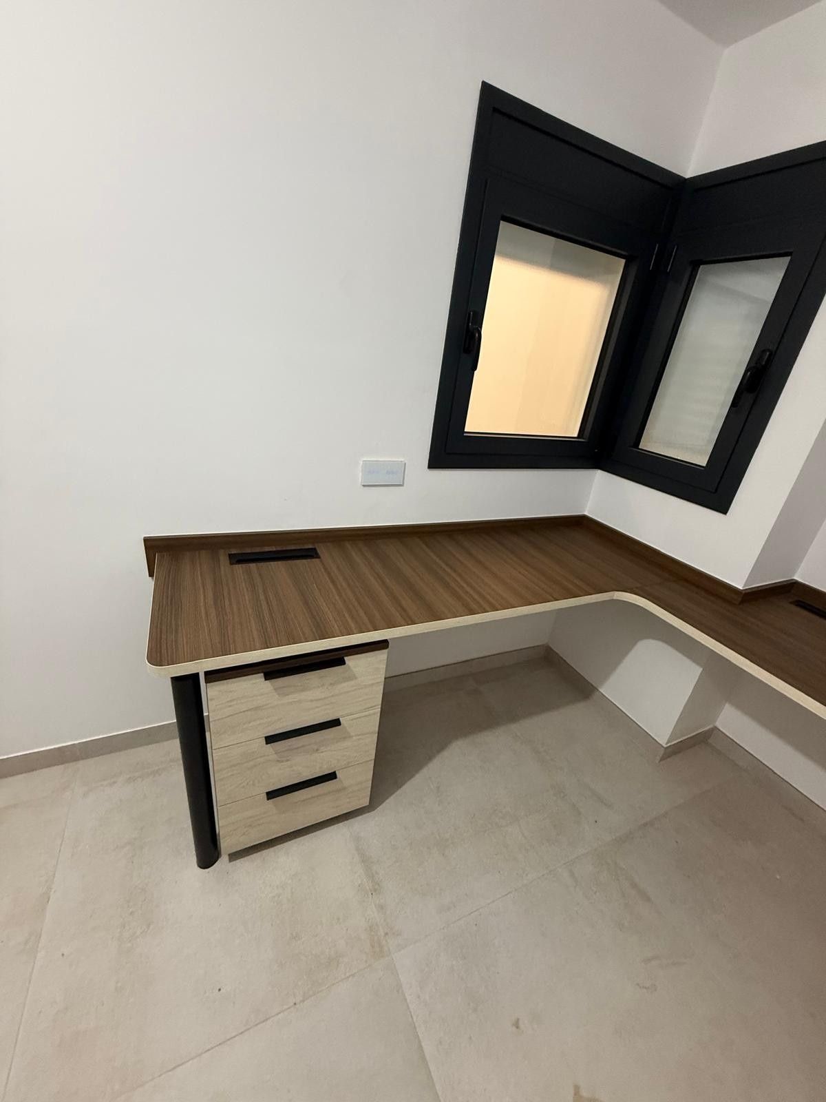 Escritorio moderno integrado en una habitación de esquina, con tablero de madera, cajones
