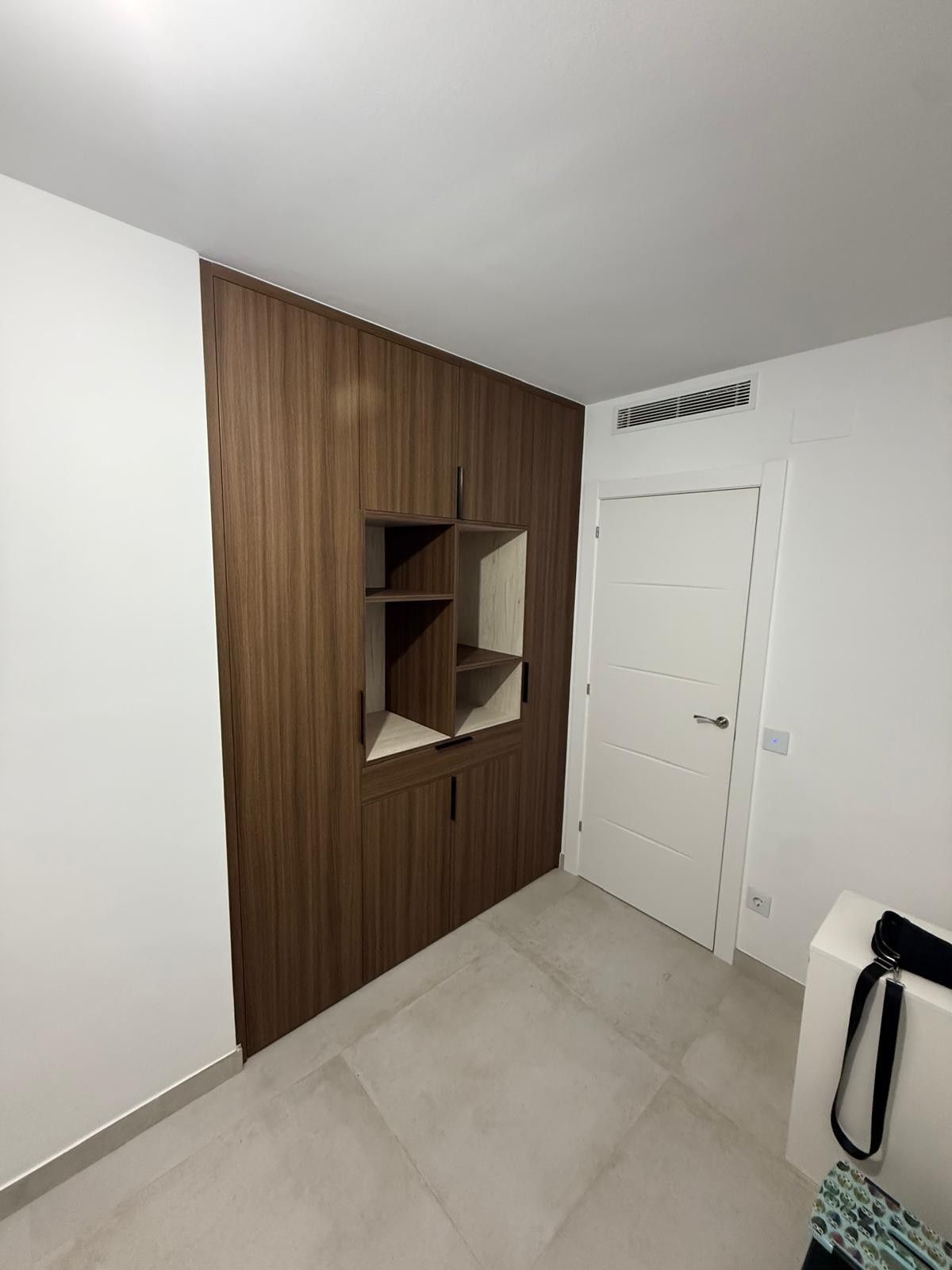 Entrada moderna con pared decorativa de madera, estantes empotrados, puerta blanca y suelo de baldosas claras.