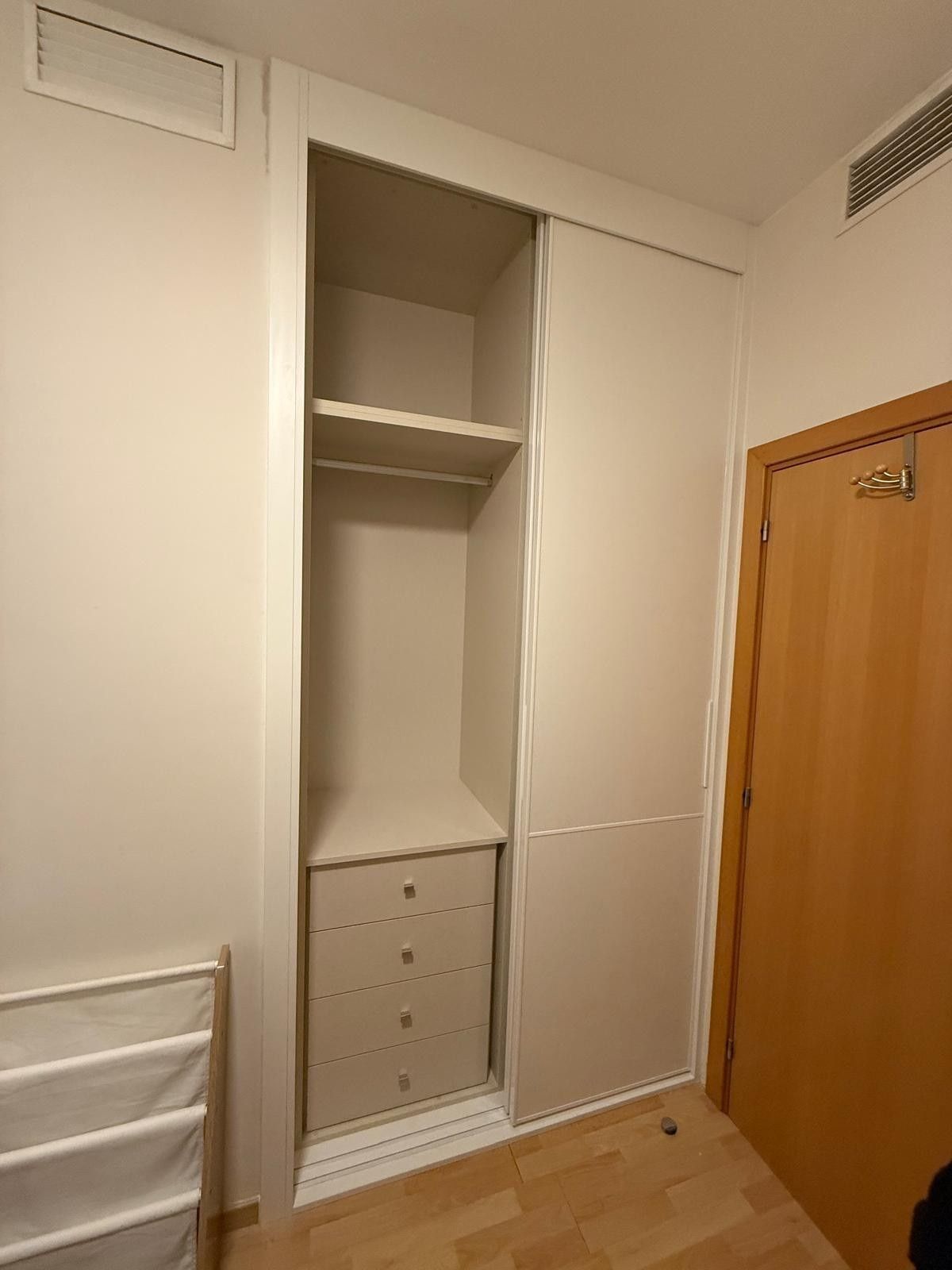 Armario empotrado con estantes abiertos y cajones en una pequeña habitación junto a una puerta de madera.