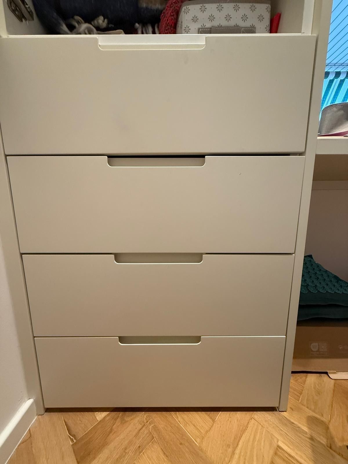 Cómoda blanca de cuatro cajones en una habitación con suelo de madera.