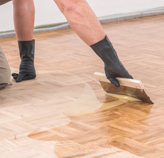 Eine Person poliert einen Holzboden mit einem Spachtel.