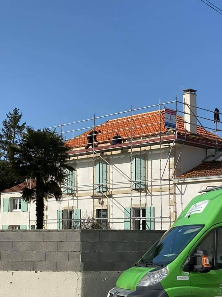 Des ouvriers, juchés sur des échafaudages, effectuent des réparations sur le toit d'une maison blanche à deux étages.