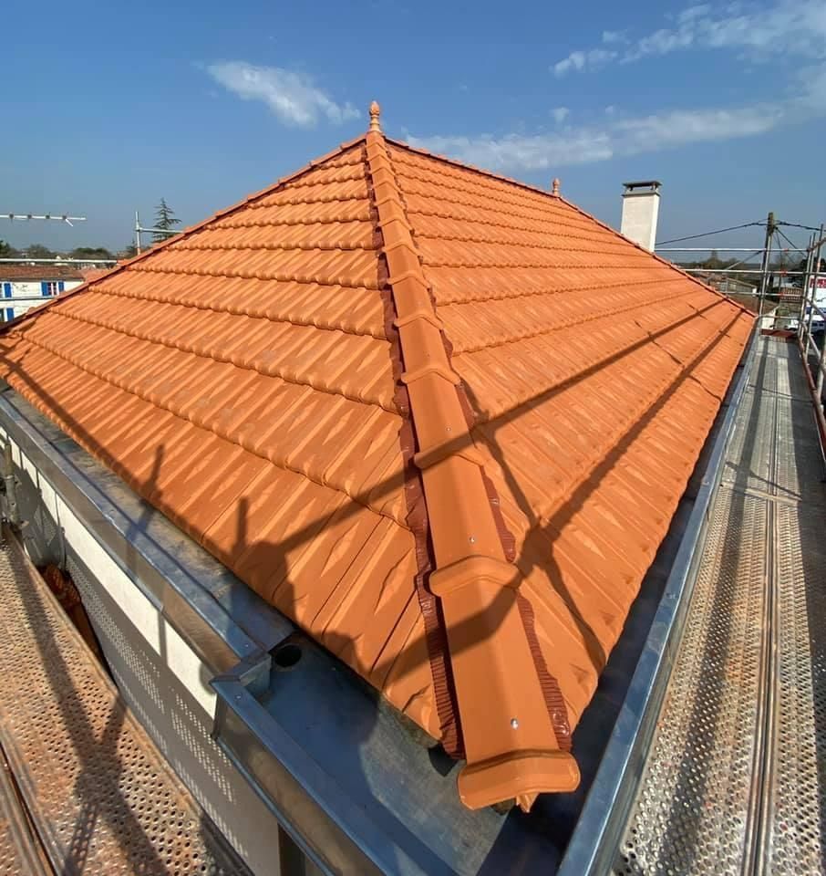 Un toit pyramidal recouvert de tuiles neuves en terre cuite orange, avec des solins métalliques.