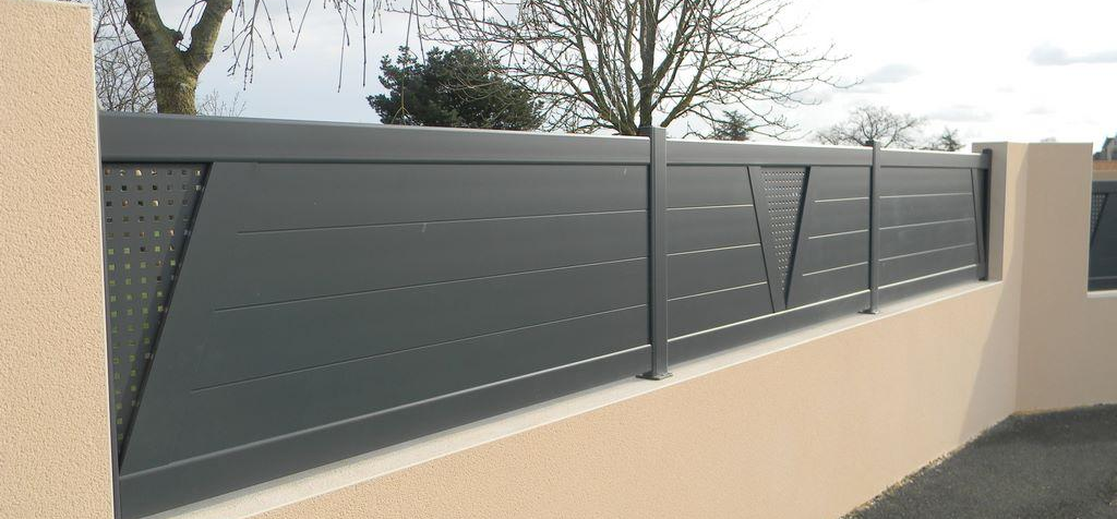 Clôture en métal gris sur un mur beige, avec des découpes décoratives en angle.