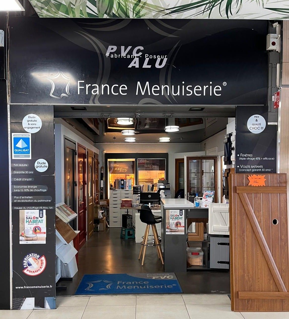 Entrée d'un magasin « France Menuiserie », avec des vitrines présentant des échantillons de menuiserie et des logos sur l'entrée.