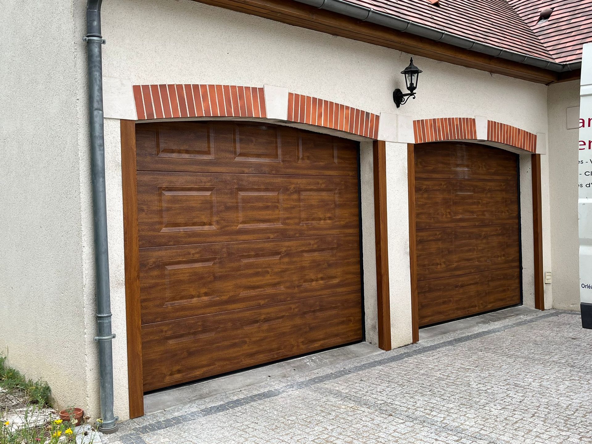 Deux portes de garage brunes avec des accents de brique sous un bâtiment couleur crème.