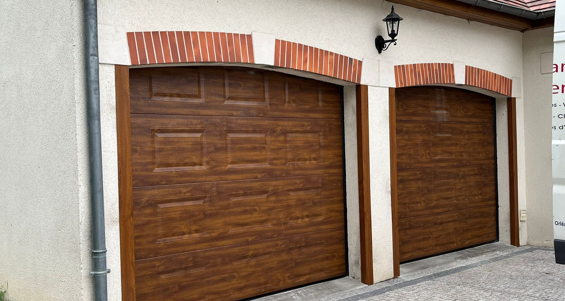 Deux portes de garage brunes avec des arcades en briques, intégrées à un bâtiment en stuc blanc.