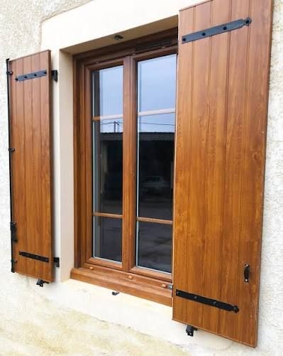 Fenêtre en bois marron avec volets ouverts sur un bâtiment beige.