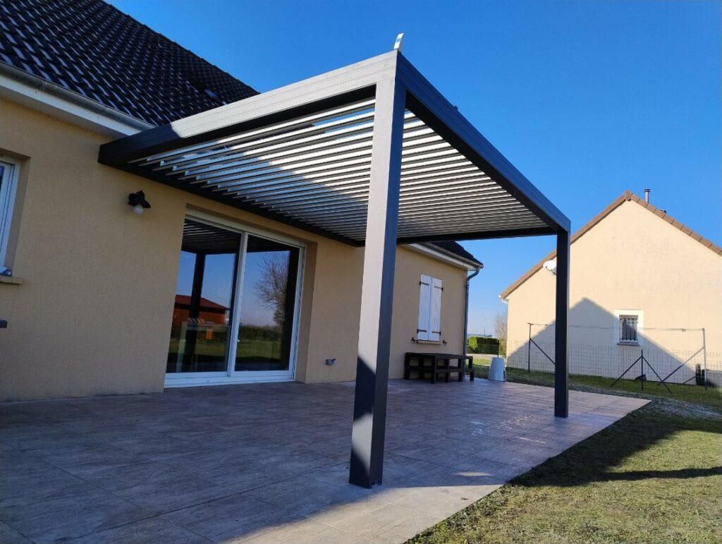 Pergola adossée à une maison beige, offrant de l'ombre à une terrasse.