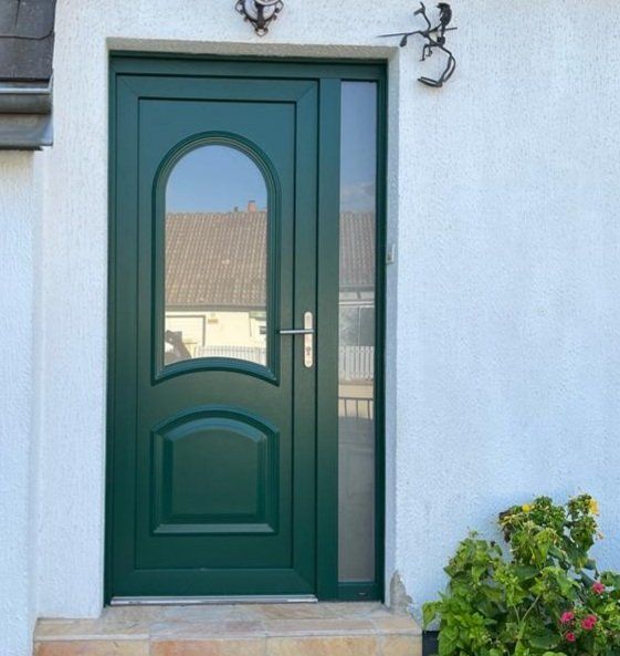 Porte d'entrée verte avec fenêtre cintrée et imposte latérale sur un mur en stuc blanc.