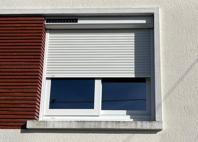 Fenêtre à volets blancs partiellement fermés, encastrée dans une façade blanche et brune.