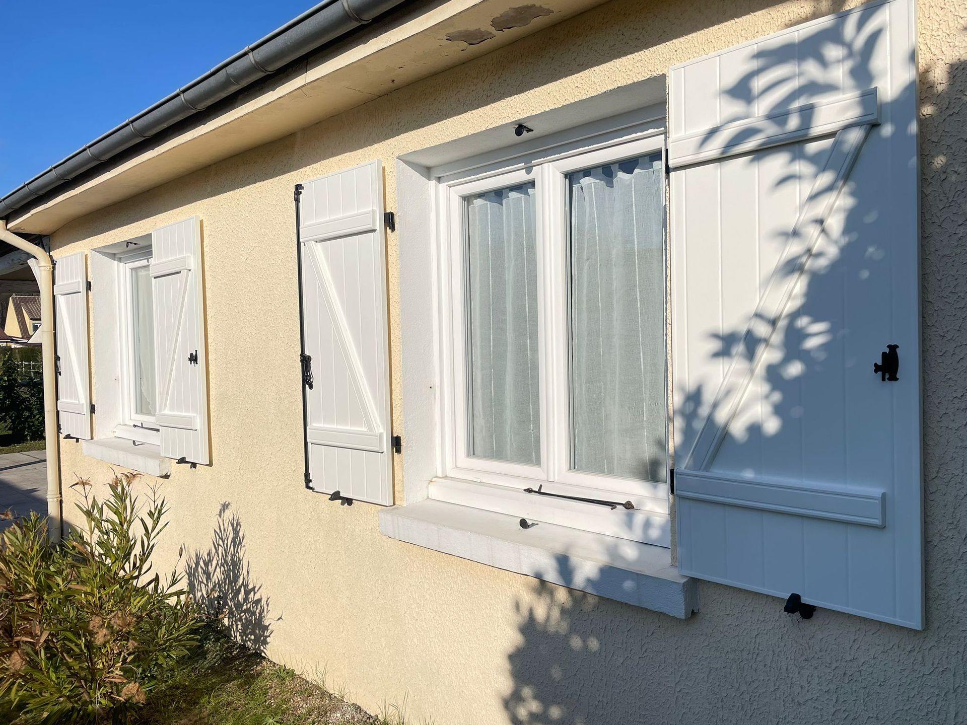 Extérieur d'une maison avec des volets gris et une porte blanche, des murs en stuc jaune et un auvent clair.