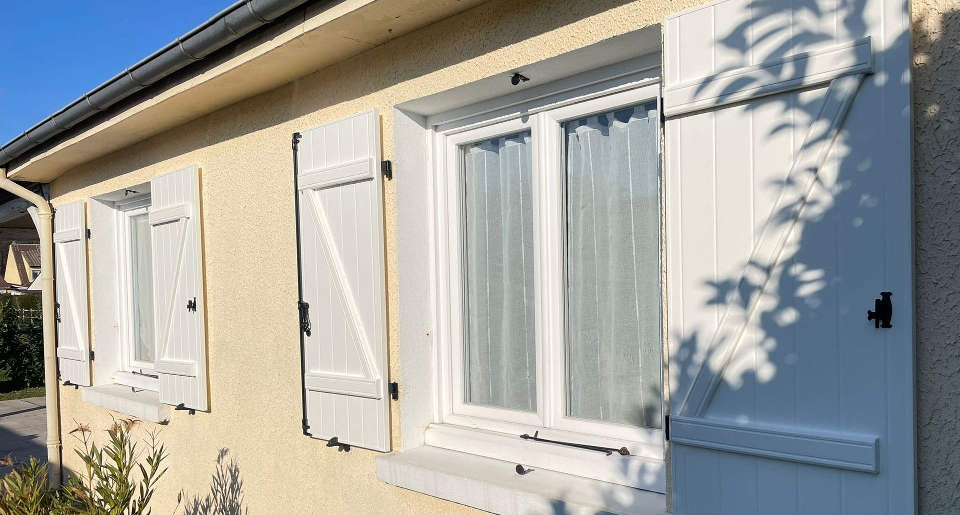 Volets blancs sur une maison en stuc jaune se détachant sur un ciel bleu.