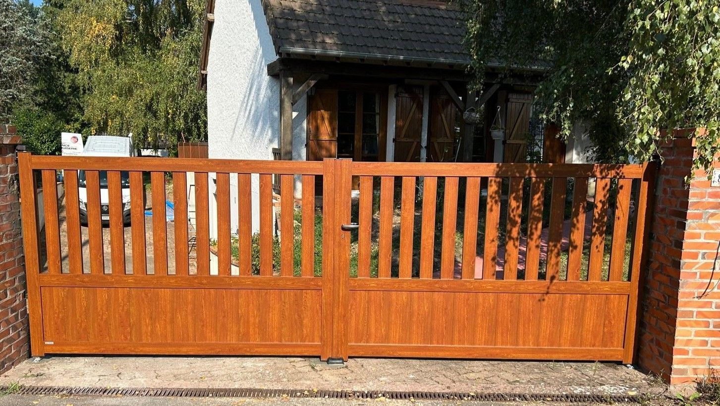 Portail double blanc à lattes verticales, piliers en briques, panneau solaire et maison.