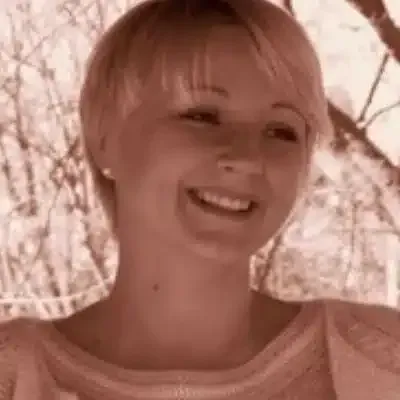 Femme souriante aux cheveux blonds courts, debout en extérieur près de branches dénudées