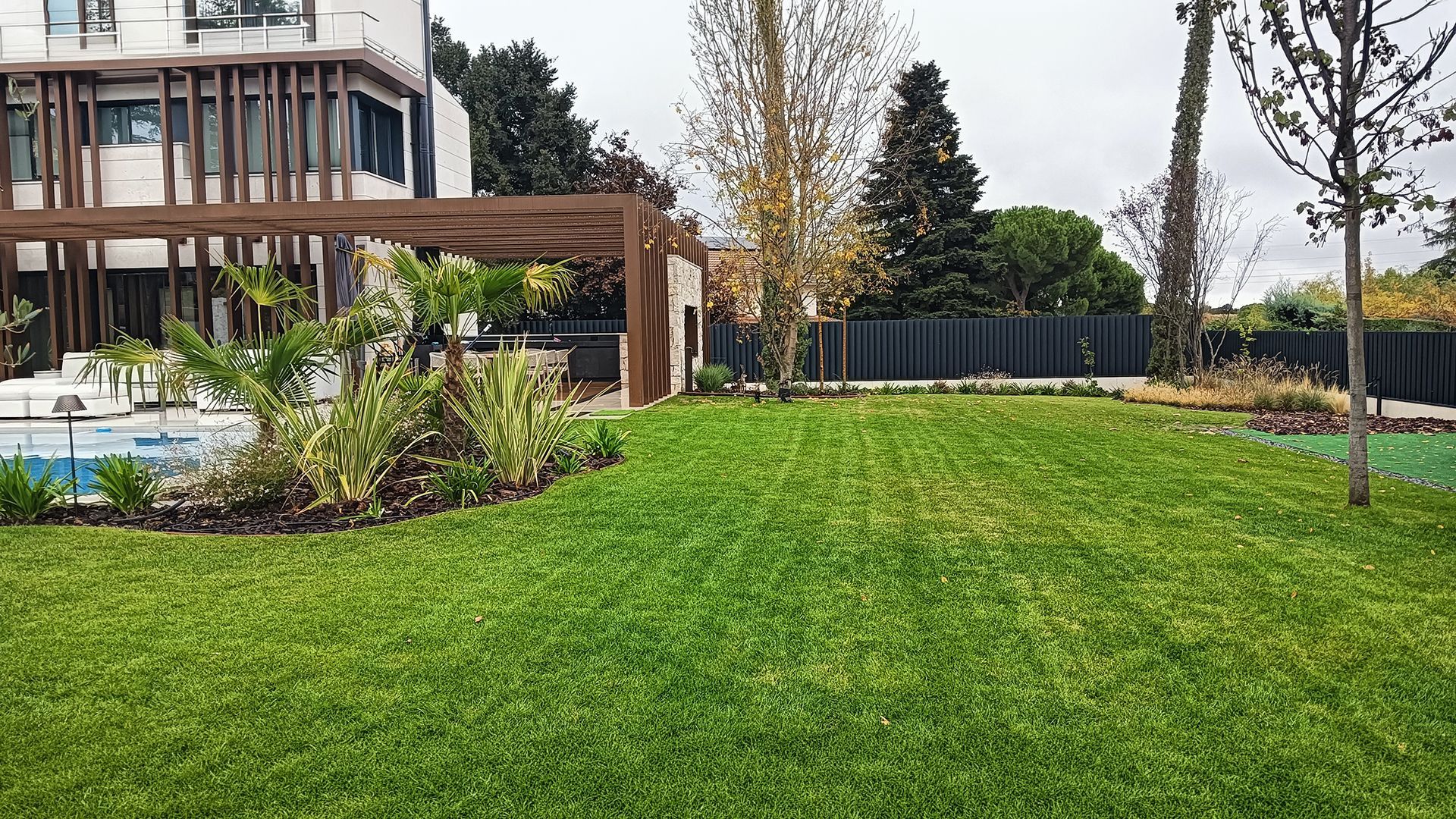 Moderno césped de jardín junto a una piscina y una pérgola de madera, junto a un edificio contemporáneo