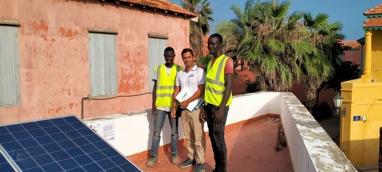 Tres hombres están parados en un tejado al lado de un panel solar.