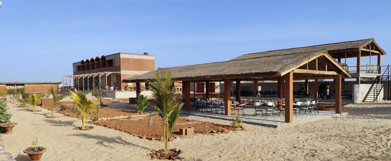 Edificio industrial rural con un refugio de madera, patio de grava y paisaje desértico bajo un cielo azul claro.