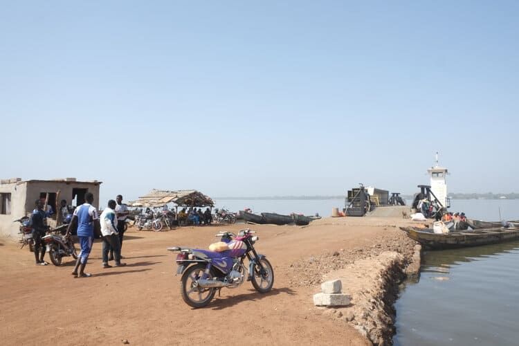 Una motocicleta está estacionada en un camino de tierra al lado de un cuerpo de agua.
