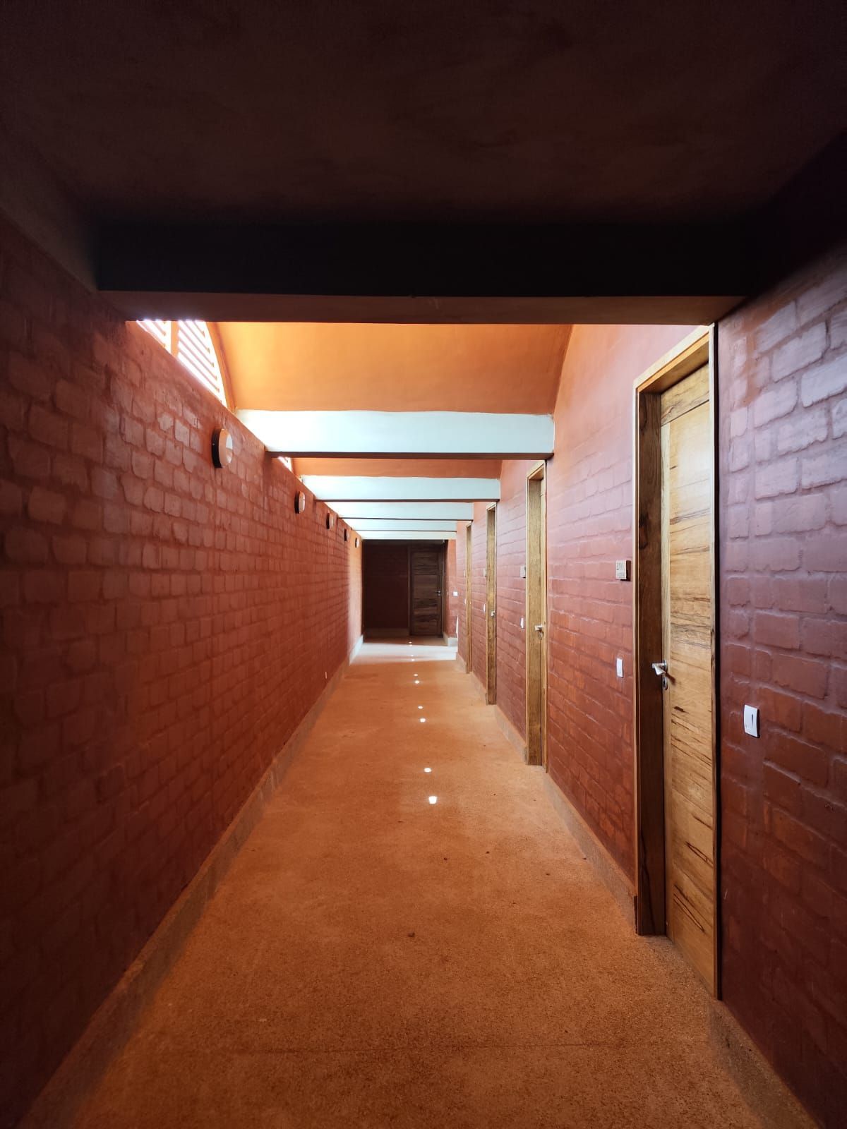 Largo pasillo de ladrillo con suelo alfombrado y puertas abiertas a la derecha.
