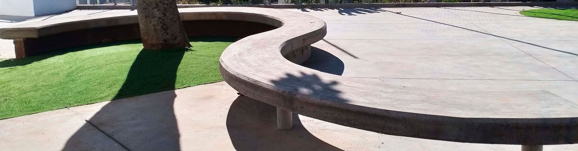 Un banco curvo en un parque con un árbol al fondo.