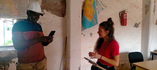 Un hombre y una mujer están parados uno al lado del otro en una habitación. La mujer sostiene un portapapeles.