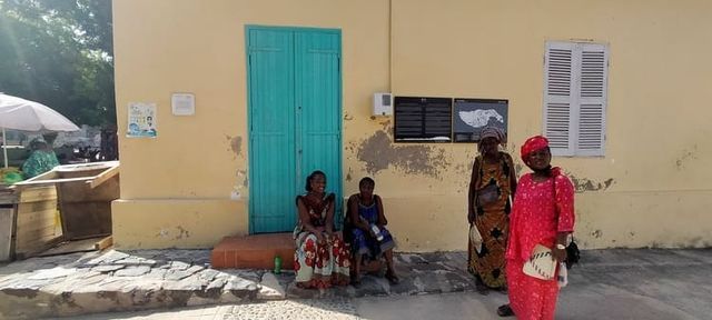 Un grupo de personas está sentado frente a un edificio amarillo con una puerta azul.