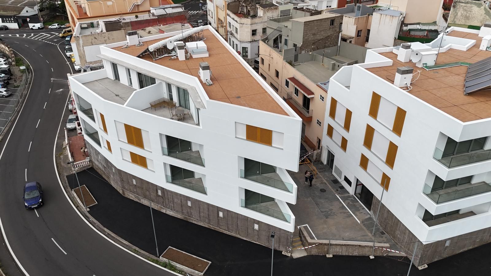Vista aérea de modernos edificios de apartamentos blancos en una calle curva de un barrio urbano densamente poblado.