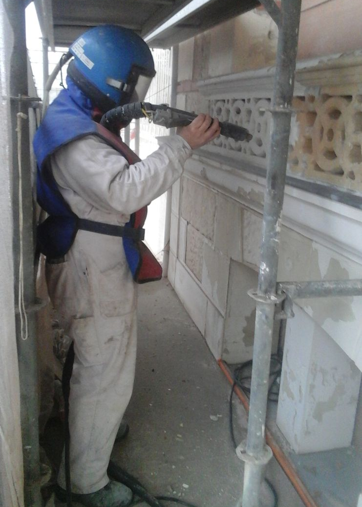 Terrasse extérieure en construction ; mur en pierre, sol en béton, carrelage et outils visibles.