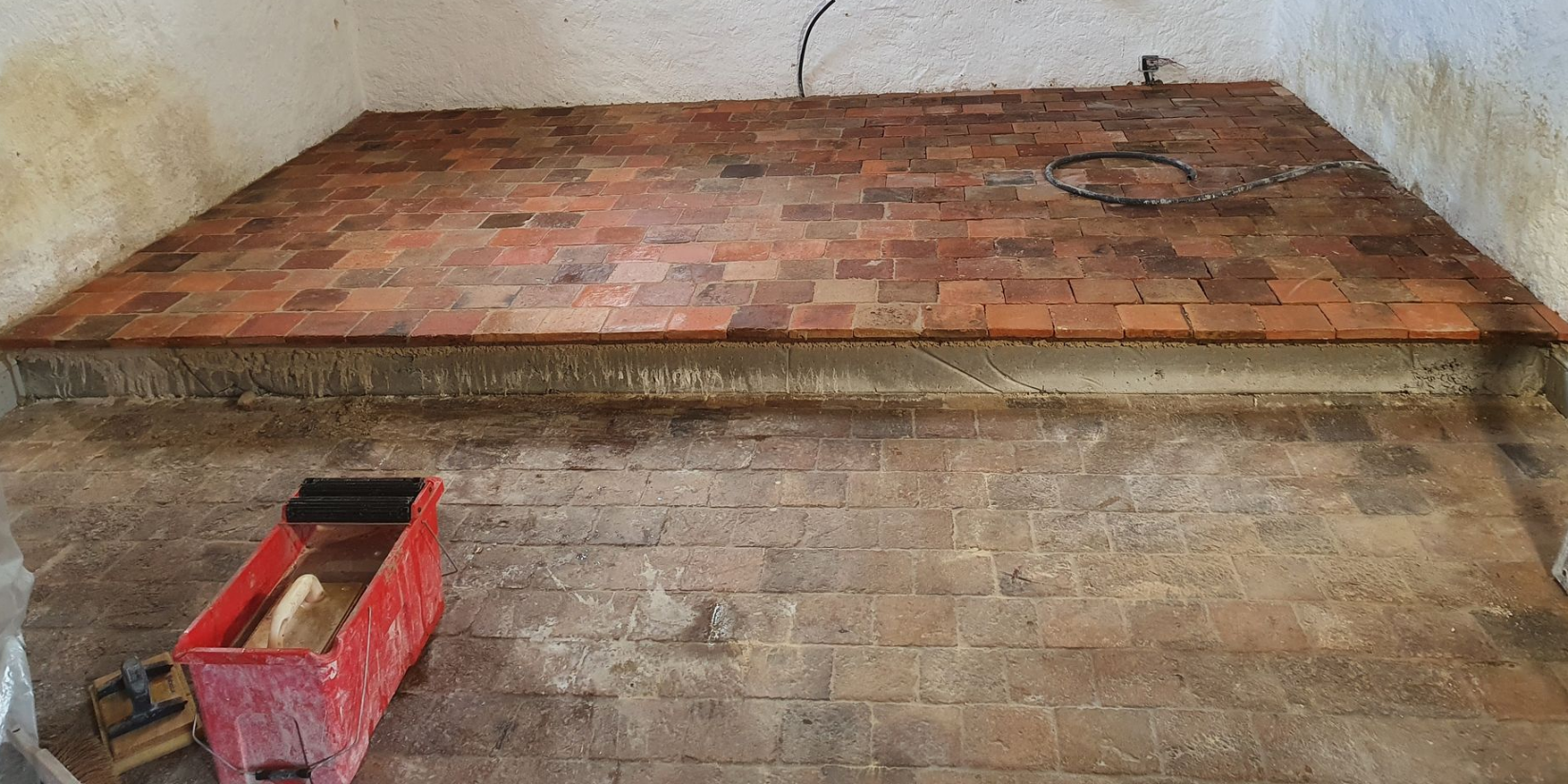 Terrasse carrelée en pierre avec surface humide, attenante à un bâtiment et un balcon.